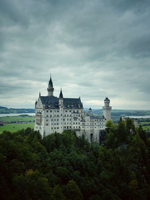 Free A captivating view of Neuschwanstein Castle surrounded by lush forests and cloudy skies in Bavaria, Germany. Stock Photo