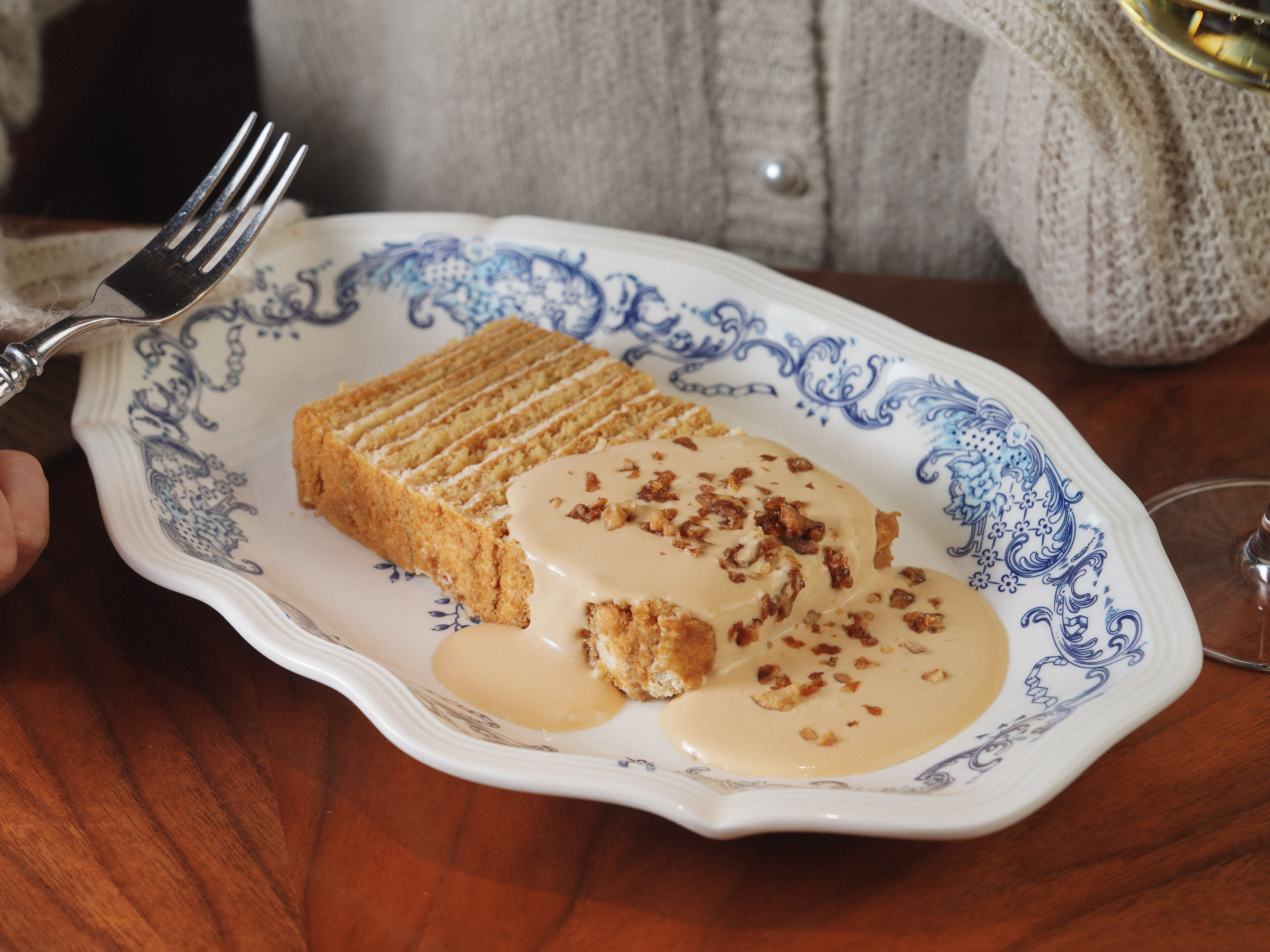 A two-layer caramel cake on a cake stand with thick caramel frosting on top and sides, one slice cut to show the tender crumb inside.