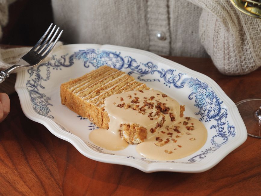 A two-layer caramel cake on a cake stand with thick caramel frosting on top and sides, one slice cut to show the tender crumb inside.