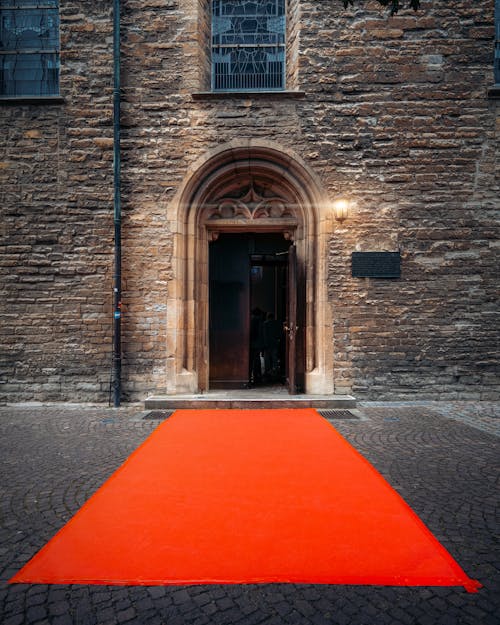 Orange Carpet Pathway Leading To The Doorway Of Brown Concrete Building With A Illuminated Wall Lamp
