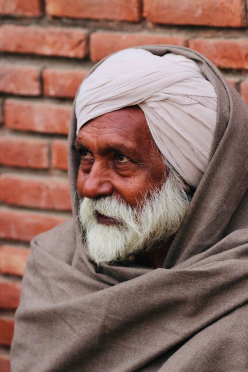 Free Close-up portrait of an elderly man wearing traditional Indian turban and shawl against a brick wall. Stock Photo