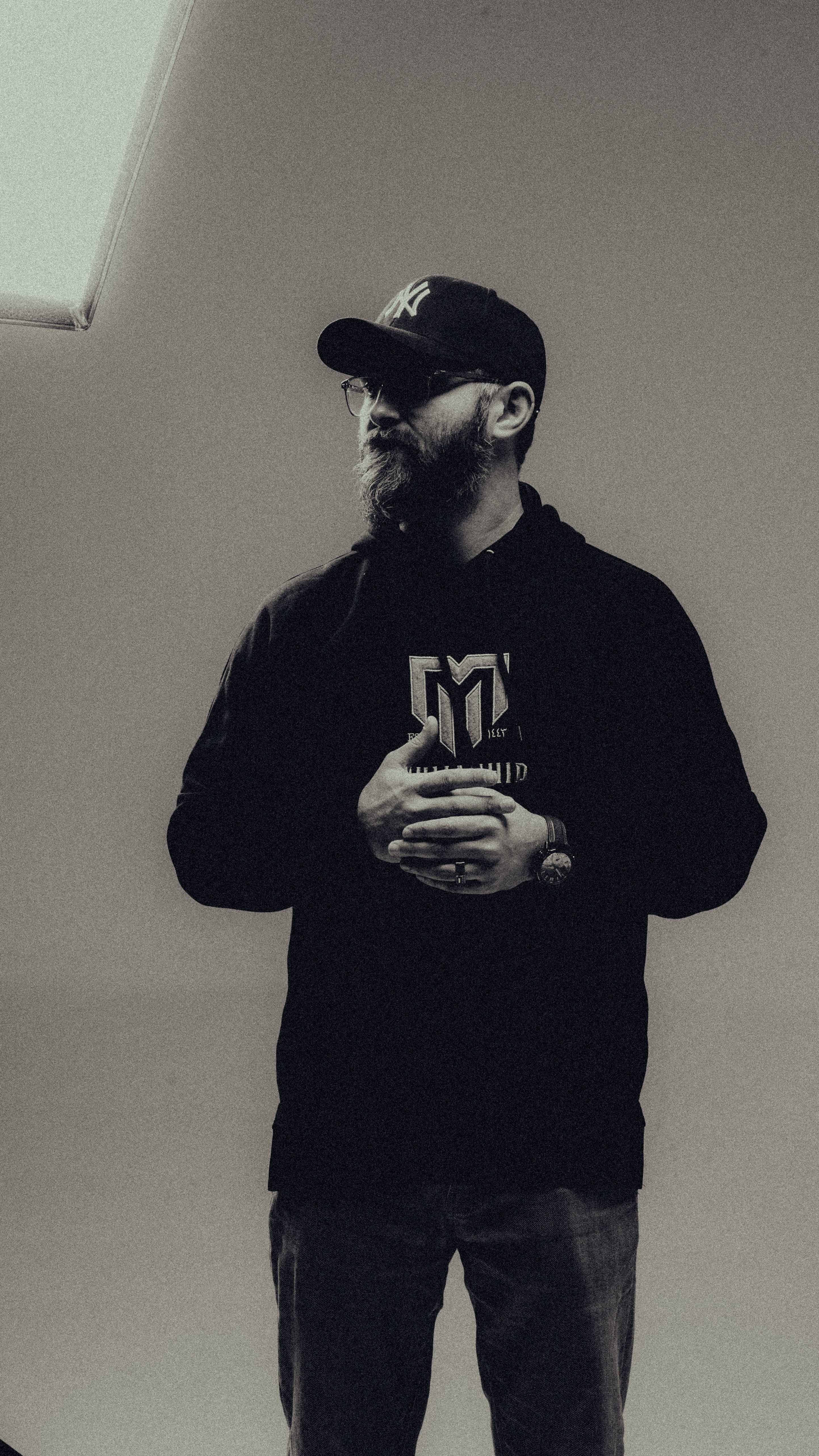 Black and white portrait of a man with a beard and cap in a studio setting.