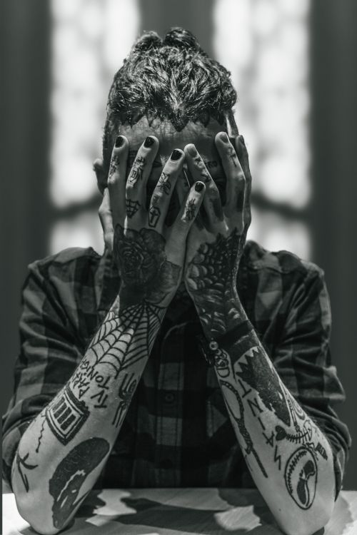 Free A black and white photo of a person with tattoos covering their face with hands. Stock Photo