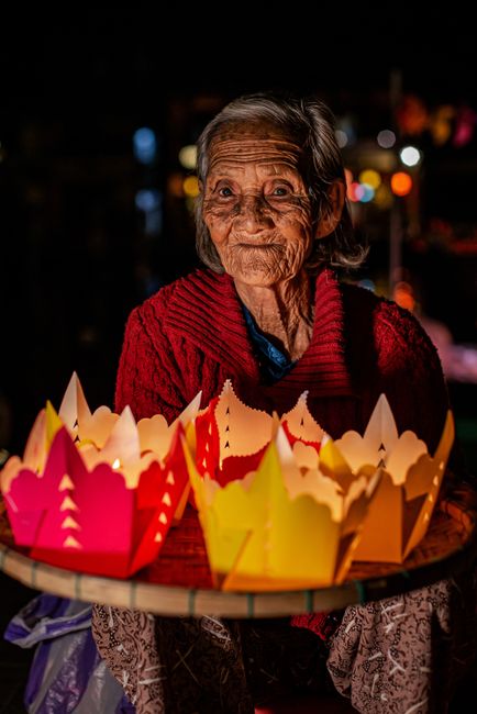A senior woman selling colorful paper lanterns at night in Hội An, Việt Nam.
