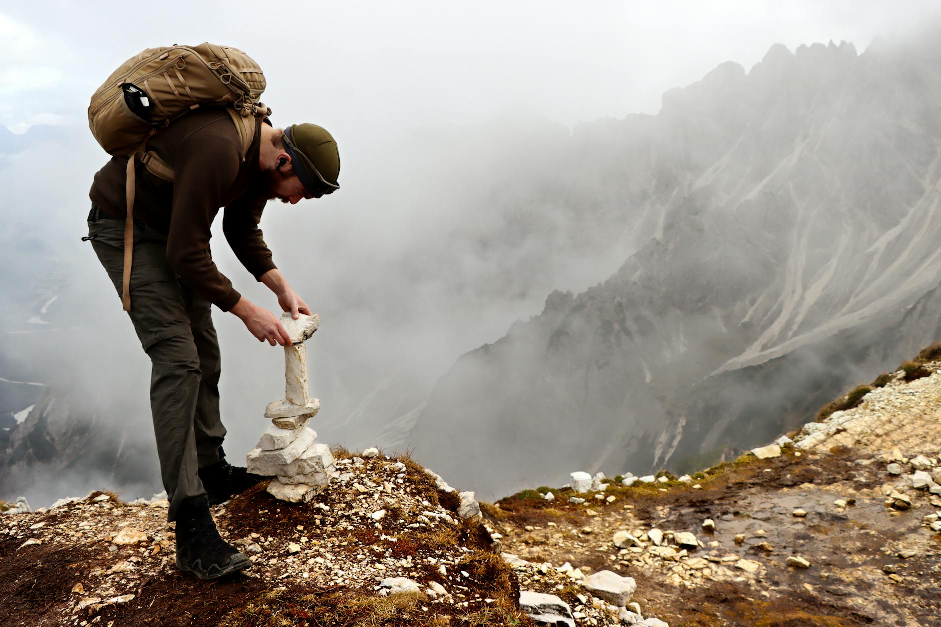 A hiker balances stones on a foggy mountain peak, showcasing mindfulness and nature exploration.