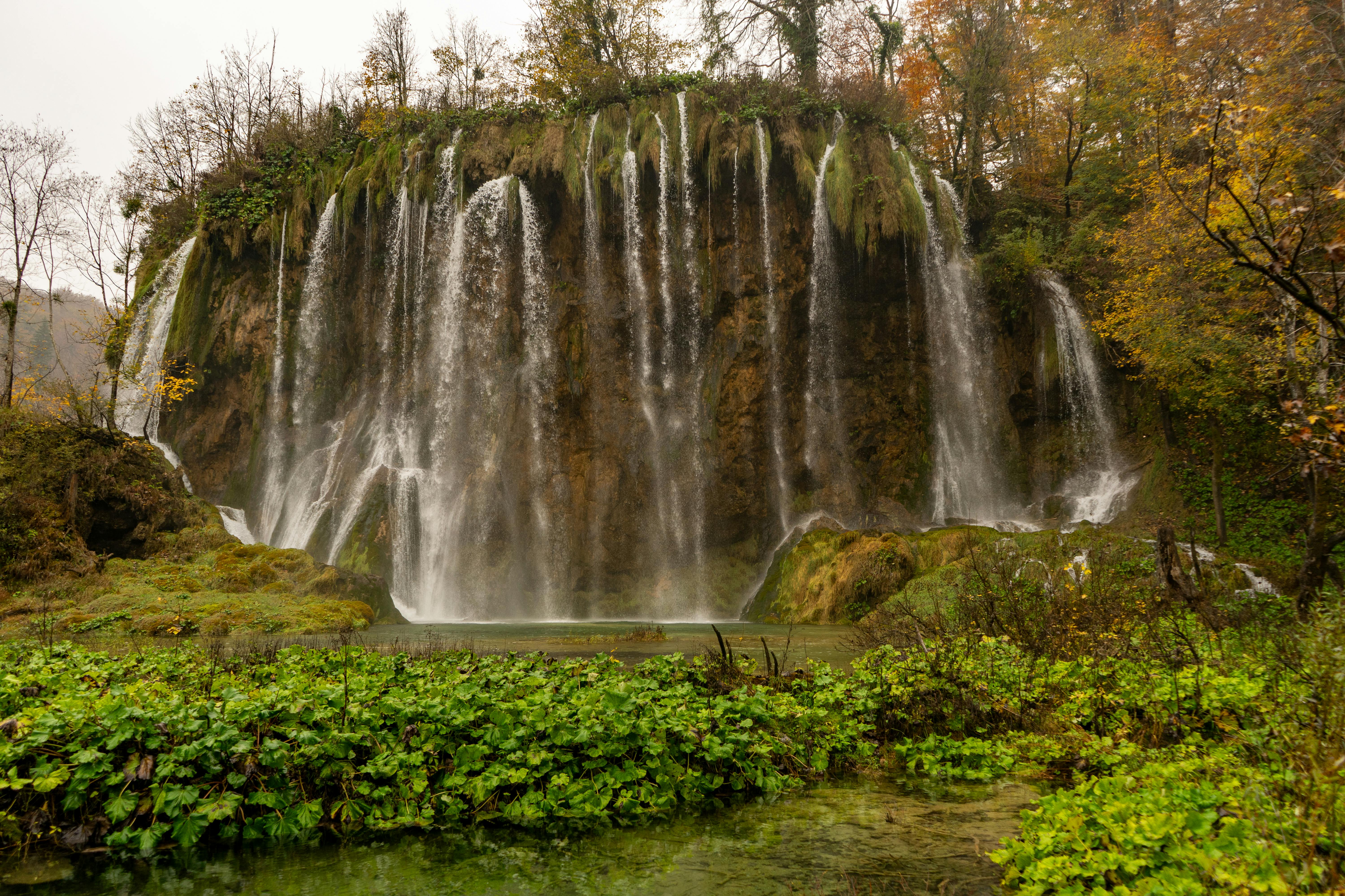 A breathtaking view of a waterfall surrounded by lush autumn foliage in Plitvice Lakes National Park, Croatia.