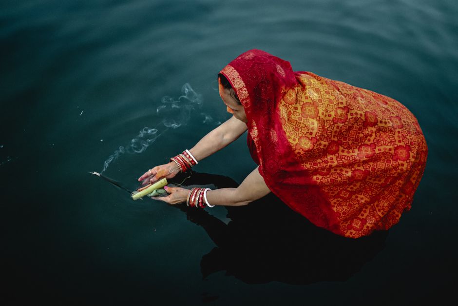 A woman in traditional attire performs Chhath Puja on a water body.
