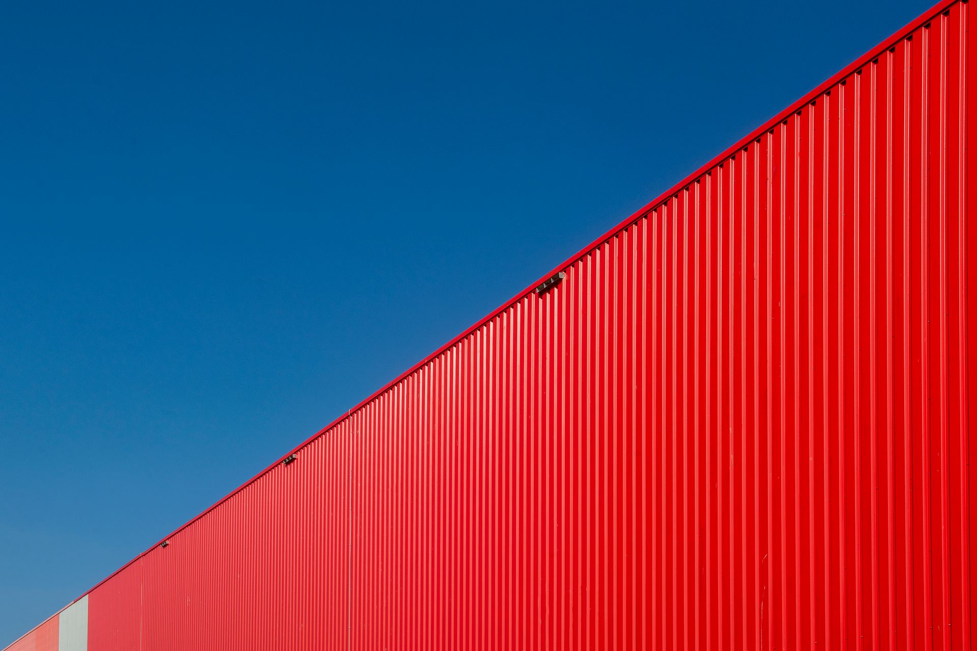An industrial red metal wall with a blue sky backdrop, creating a striking visual contrast.