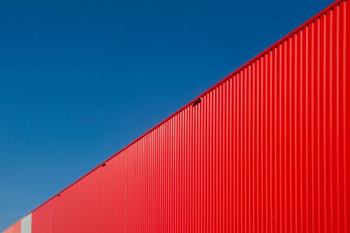 Free An industrial red metal wall with a blue sky backdrop, creating a striking visual contrast. Stock Photo