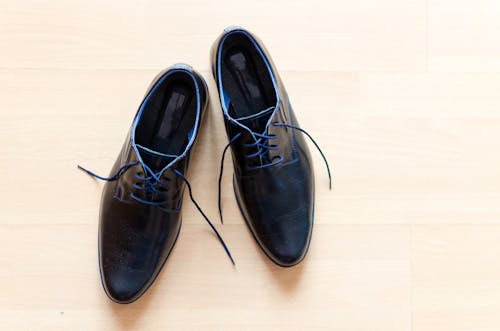 Par De Zapatos Derby De Cuero Negro Colocados Sobre Una Superficie Marrón