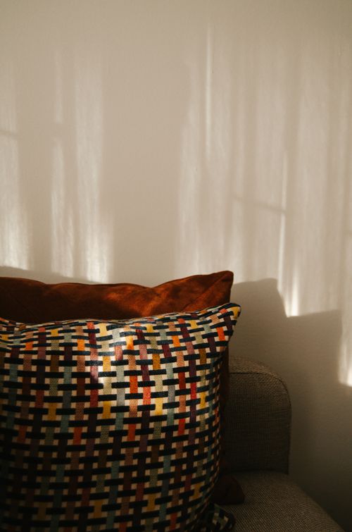 Free Warm sunlight casts shadows on a colorful cushion resting on a modern sofa, creating a cozy indoor atmosphere. Stock Photo