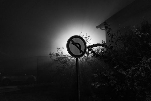Dramatic silhouette of a no-left-turn sign in foggy night light.
