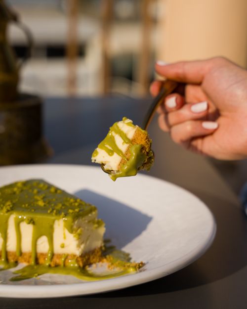Free Close-up of hand holding a fork with a matcha cheesecake slice, garnished with green glaze. Stock Photo