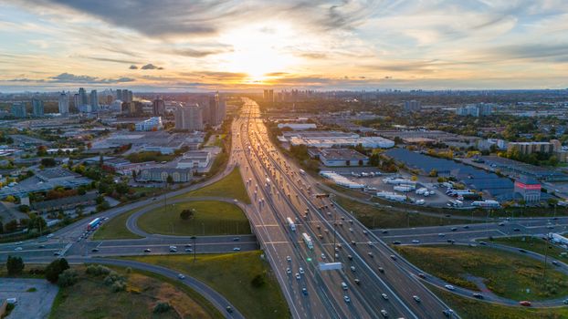 Dramatic aerial view of a busy highway in Toronto at sunset with cityscape background.