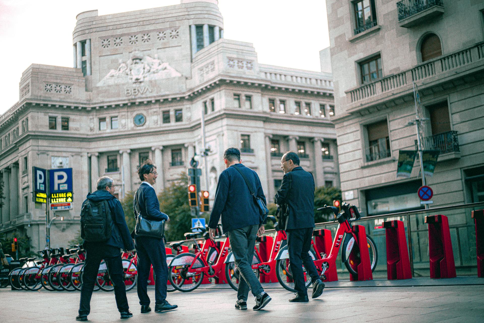 A group of men stand near shared bicycles in front of a historic bank building.