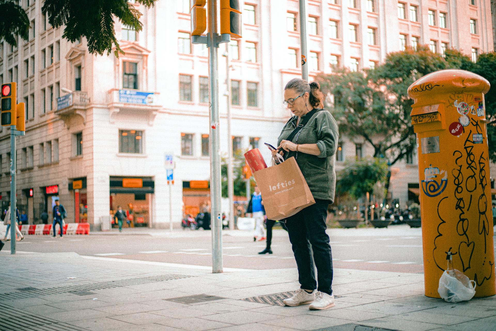 Woman with shopping bag beside vibrant urban mailbox in a city street.