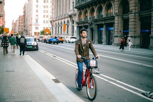 Free A man rides a bicycle in a busy city street, surrounded by historic architecture. Stock Photo