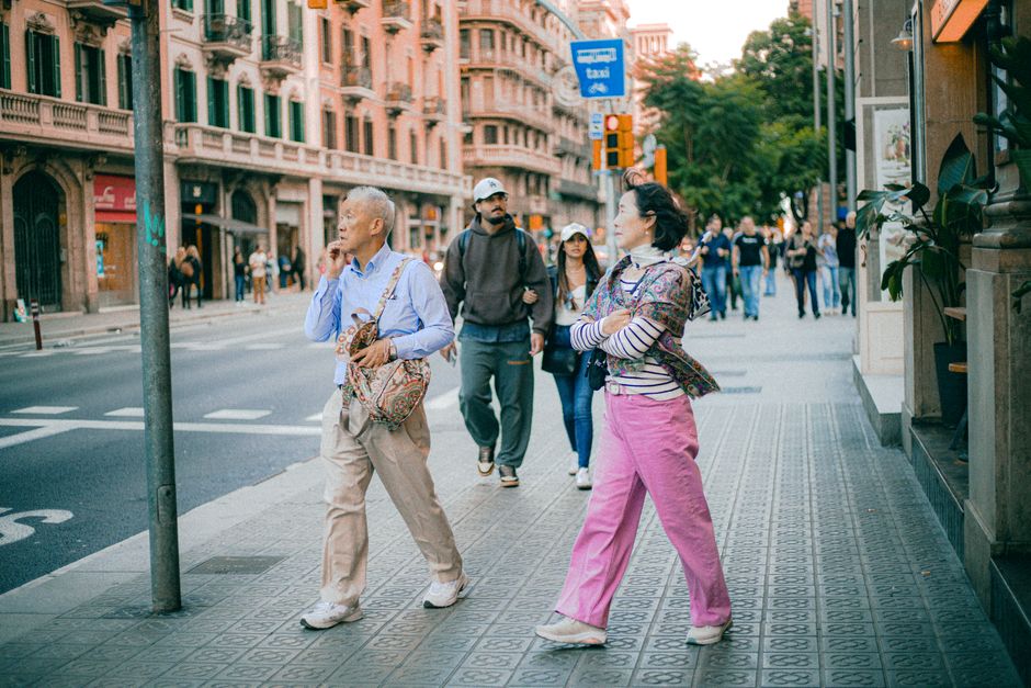 Pareja de ancianos caminando por una vibrante calle de la ciudad, rodeada de gente y arquitectura histórica.