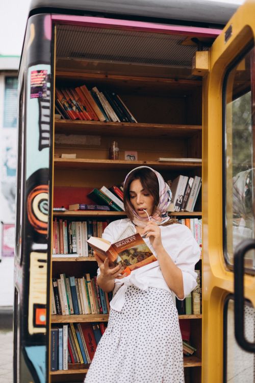 Free A woman reading a book in a colorful, outdoor mini library. Stock Photo