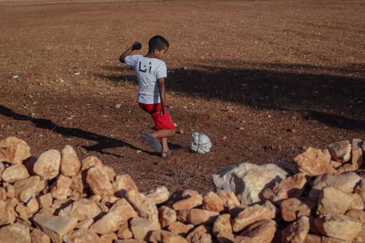 Boy in Safi, Morocco, playing football on a dry field. Captures youthful spirit.