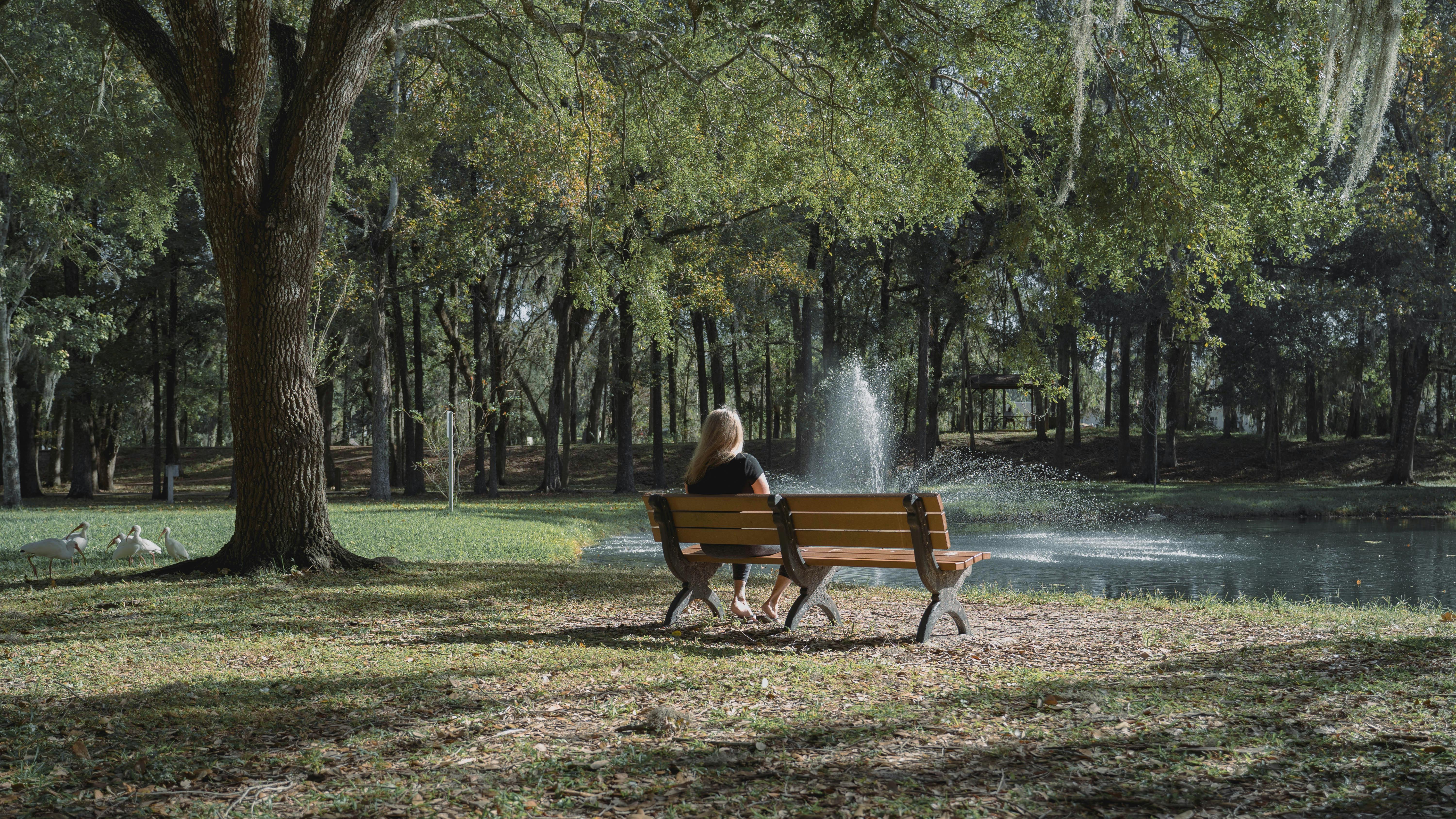 Peaceful park scene with a woman on a bench by a pond and fountain in Brooksville, Florida.