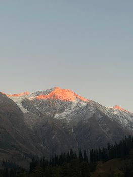 Serene view of snow-capped mountains glowing in sunset light, creating a peaceful natural scene.