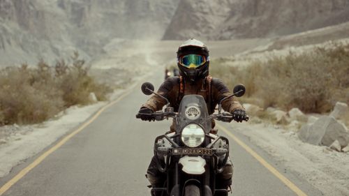 Free Motorcyclist rides through breathtaking mountain landscape wearing full protective gear. Stock Photo