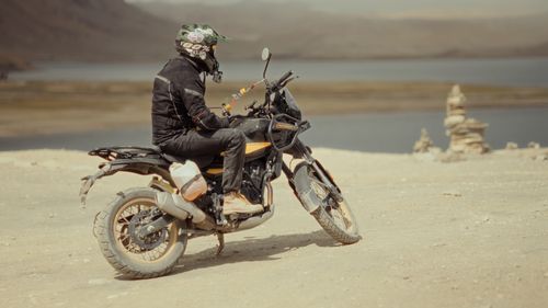 Free A motorcyclist pausing on a dirt path beside a tranquil lake amidst vast, deserted landscapes. Stock Photo