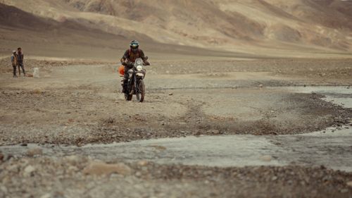 Free Motorcyclist crosses rocky terrain in a remote desert landscape, showcasing adventure travel. Stock Photo