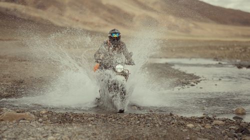 Free Motorcyclist splashes through a wild mountain stream showcasing adventure and thrill. Stock Photo