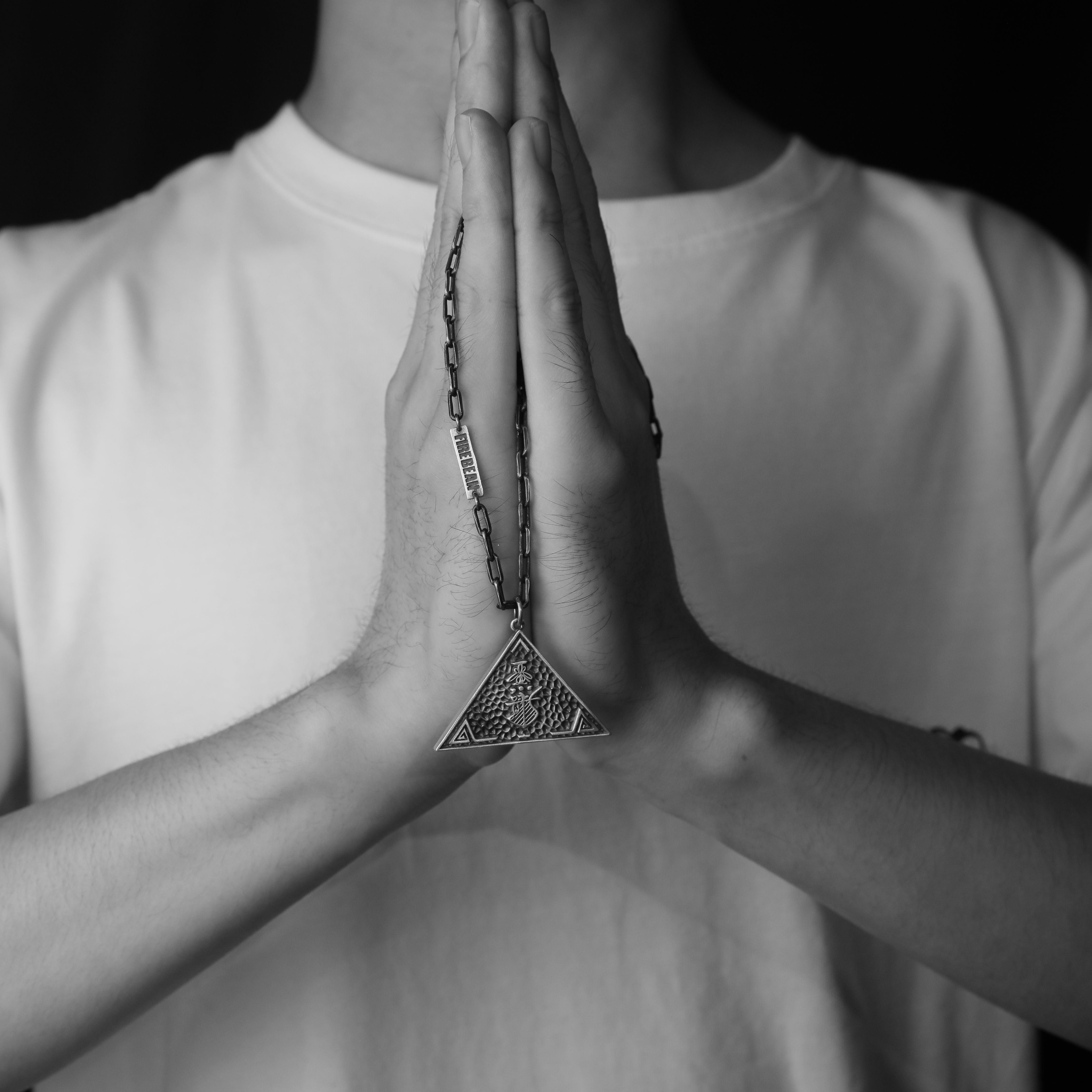 Black and white image of clasped hands in prayer with a triangle pendant.