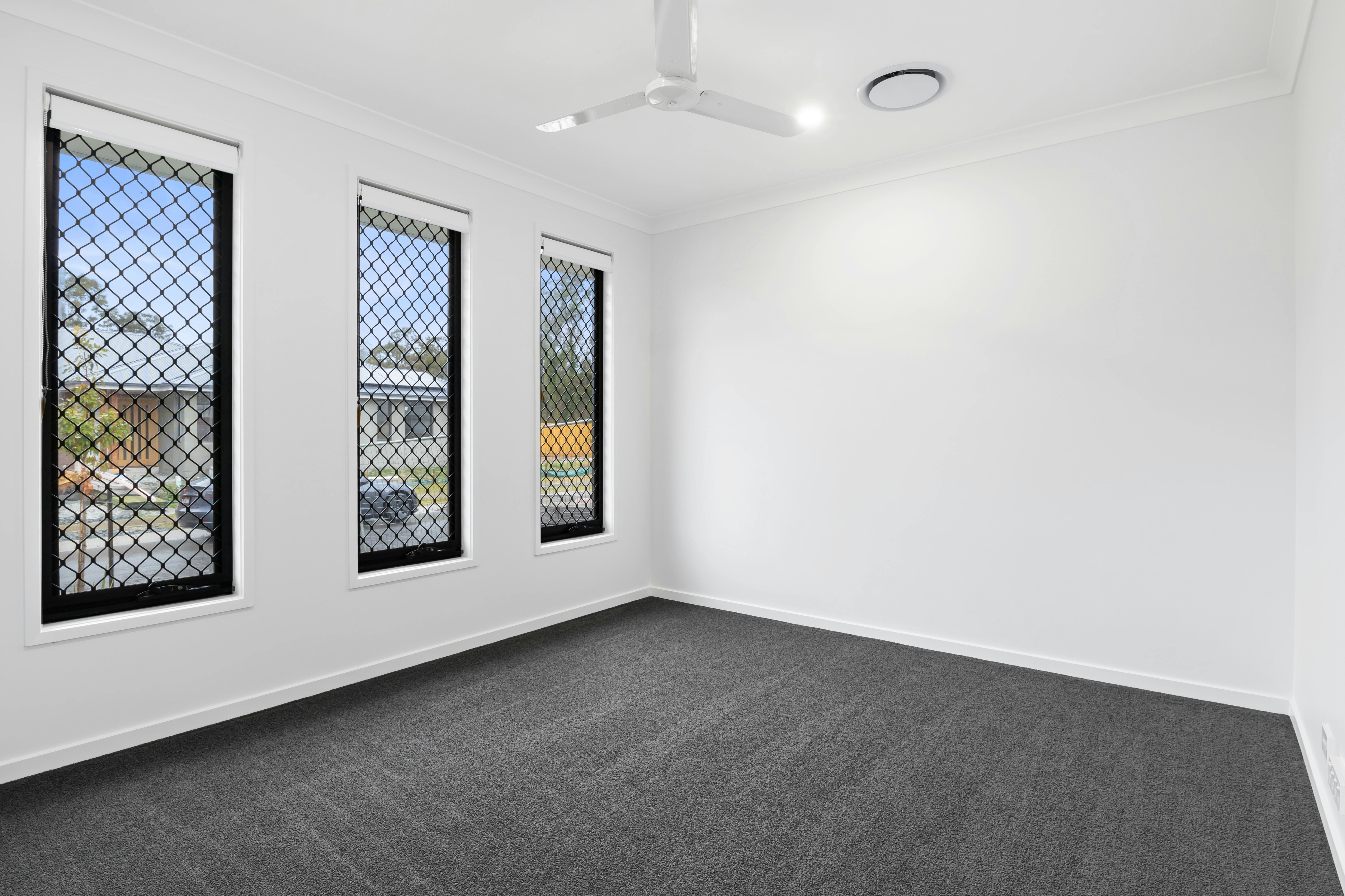 Spacious empty room with carpet, ceiling fan, and windows with security grills, located in Australia.