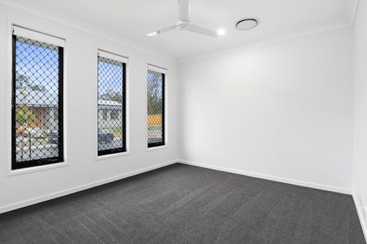 Spacious empty room with carpet, ceiling fan, and windows with security grills, located in Australia.