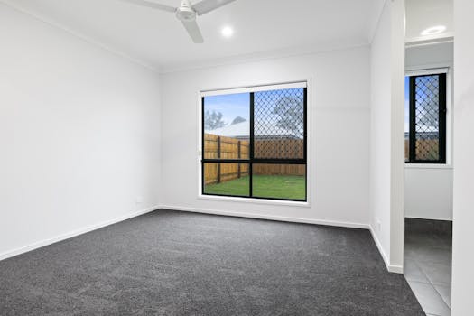 Empty room with large window and gray carpet, ideal for real estate listings.
