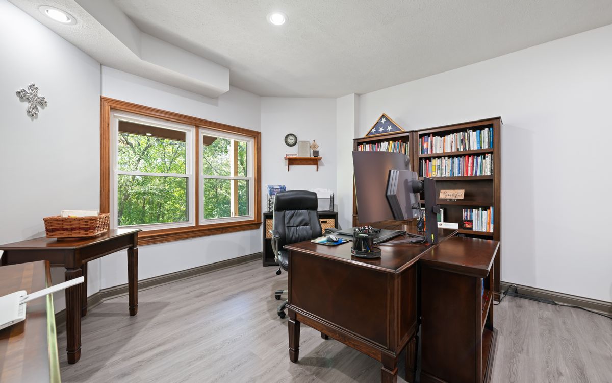 Modern home office with a warm wooden desk and bookshelves, morning light through a window overlooking greenery