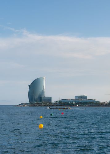 Vista panorámica del hotel W Barcelona con mar en calma y cielo azul claro.