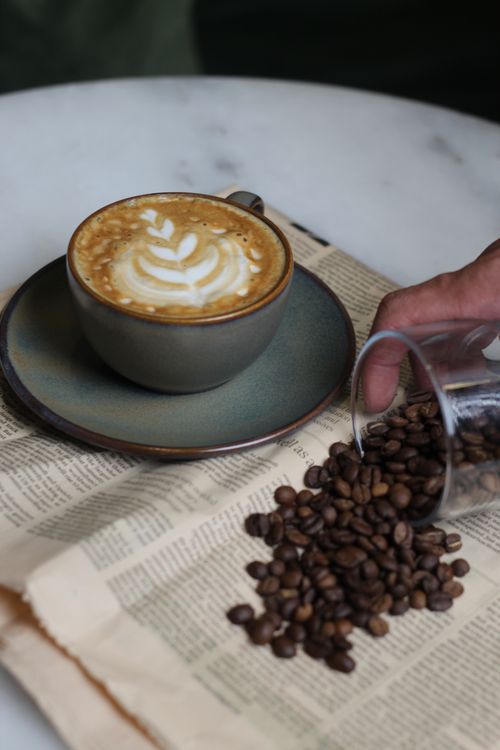 Free A cappuccino with latte art next to spilled coffee beans on a vintage newspaper. Stock Photo
