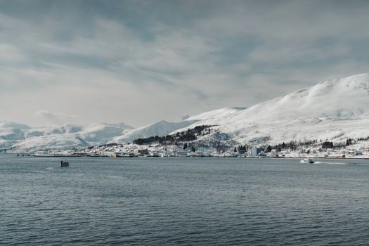 Scenic view of a snowy Norwegian village by the sea with a fishing boat.