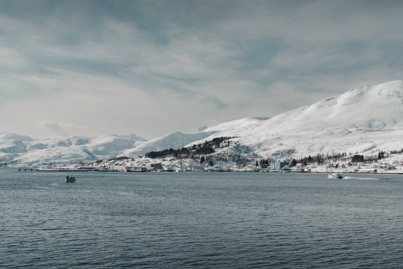 Barcă de pescuit lângă coastă norvegiană înzăpezită cu munți