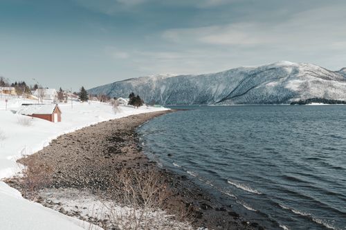 Free Beautiful snowy scene of Norway's coast with mountains and houses along the shore. Stock Photo