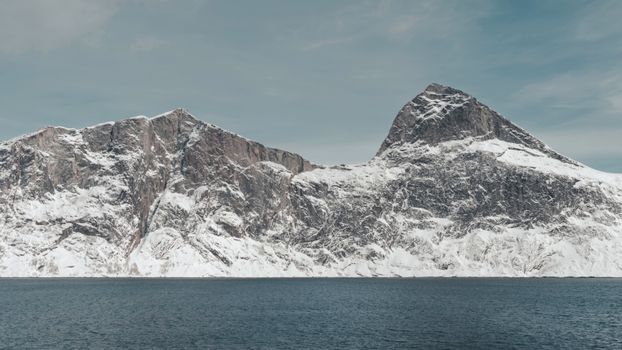 Majestic snow-covered mountains rising over the calm sea in an arctic landscape.