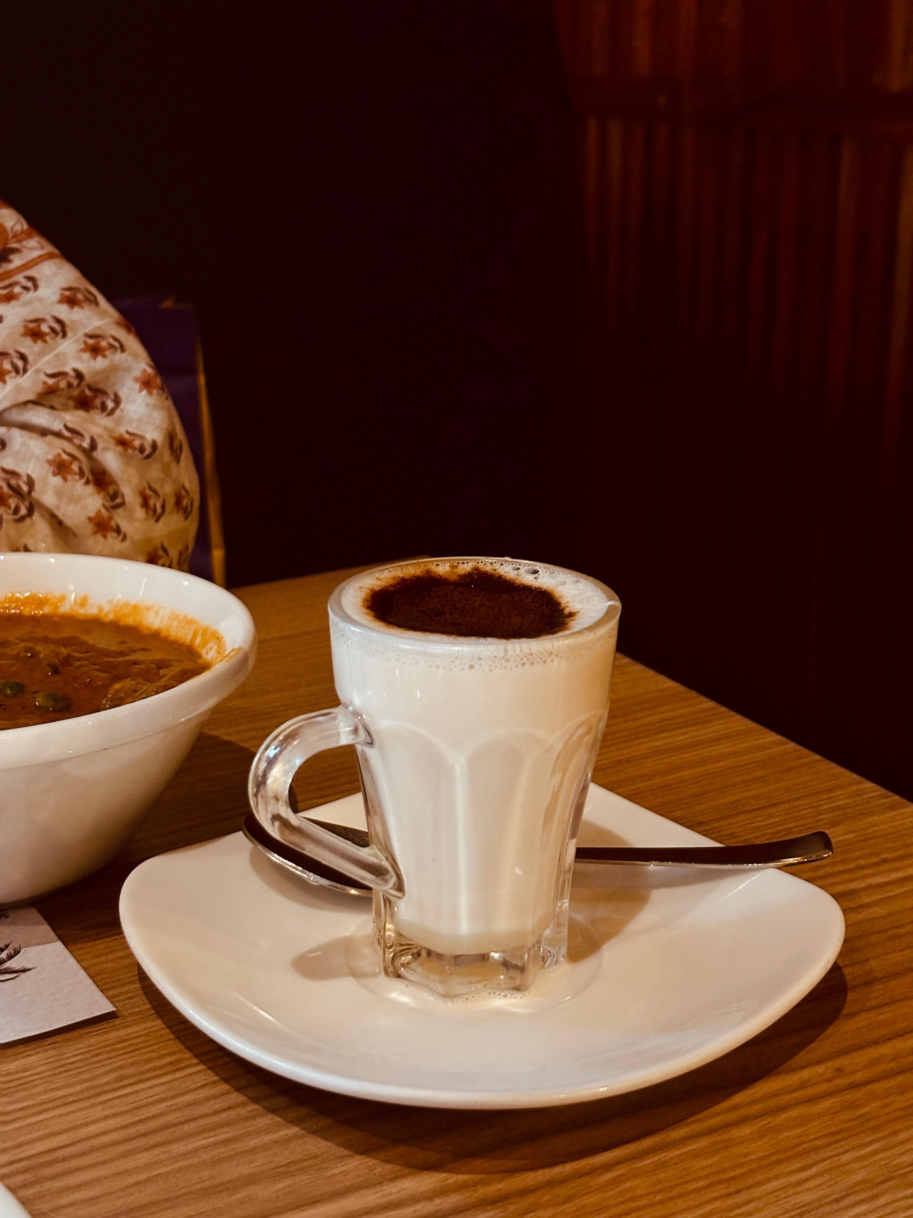 Glass of masala chai and bowl of curry on wooden table. Warm, vibrant setting.