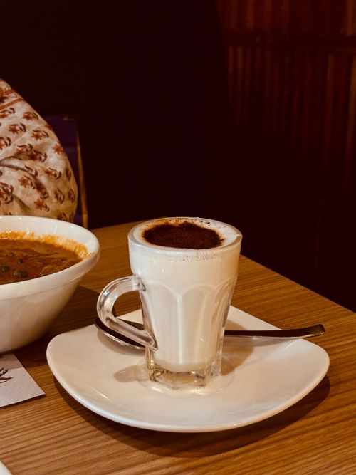 Free Glass of masala chai and bowl of curry on wooden table. Warm, vibrant setting. Stock Photo