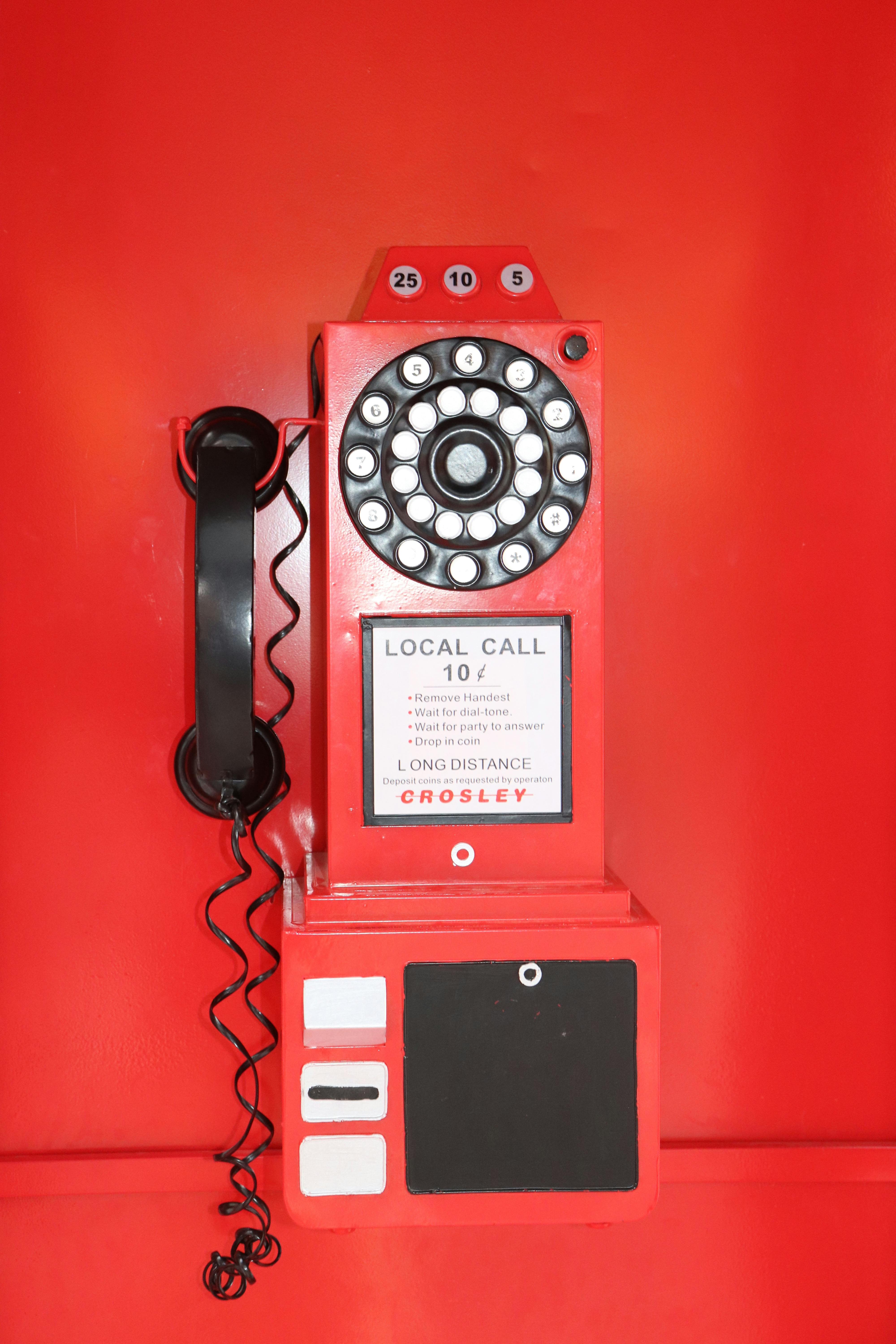 Kostenlos Ein klassisches rotes Münztelefon mit Wählscheibe vor einem leuchtend roten Hintergrund mit fettgedruckten Zahlen. Stock-Foto