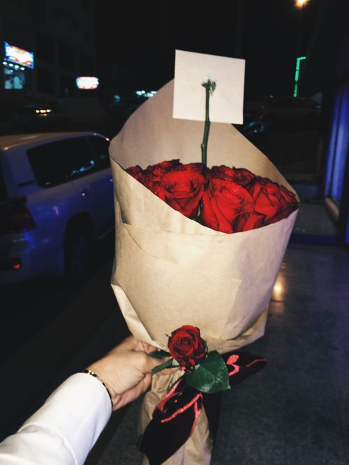 Free A bouquet of red roses in brown paper held outdoors at night in Saudi Arabia. Stock Photo