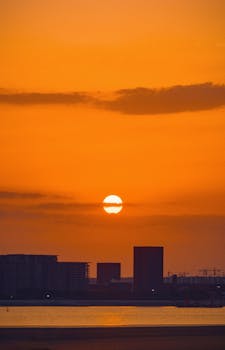 Beautiful sunset over the Hangzhou skyline with an orange sky and silhouetted buildings.