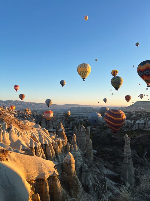 Free Colorful hot air balloons soar over Cappadocia's unique rock formations during sunrise in Türkiye. Stock Photo