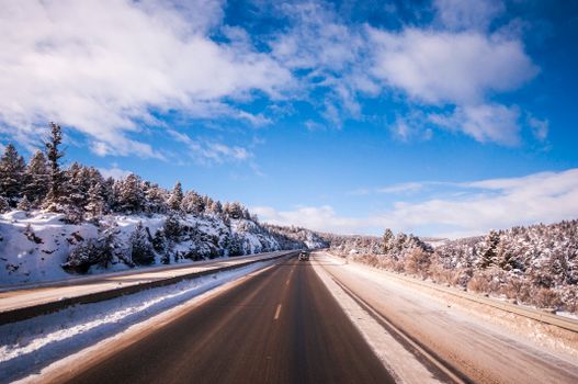 A picturesque winter highway scene flanked by snowy mountains and clear blue skies.