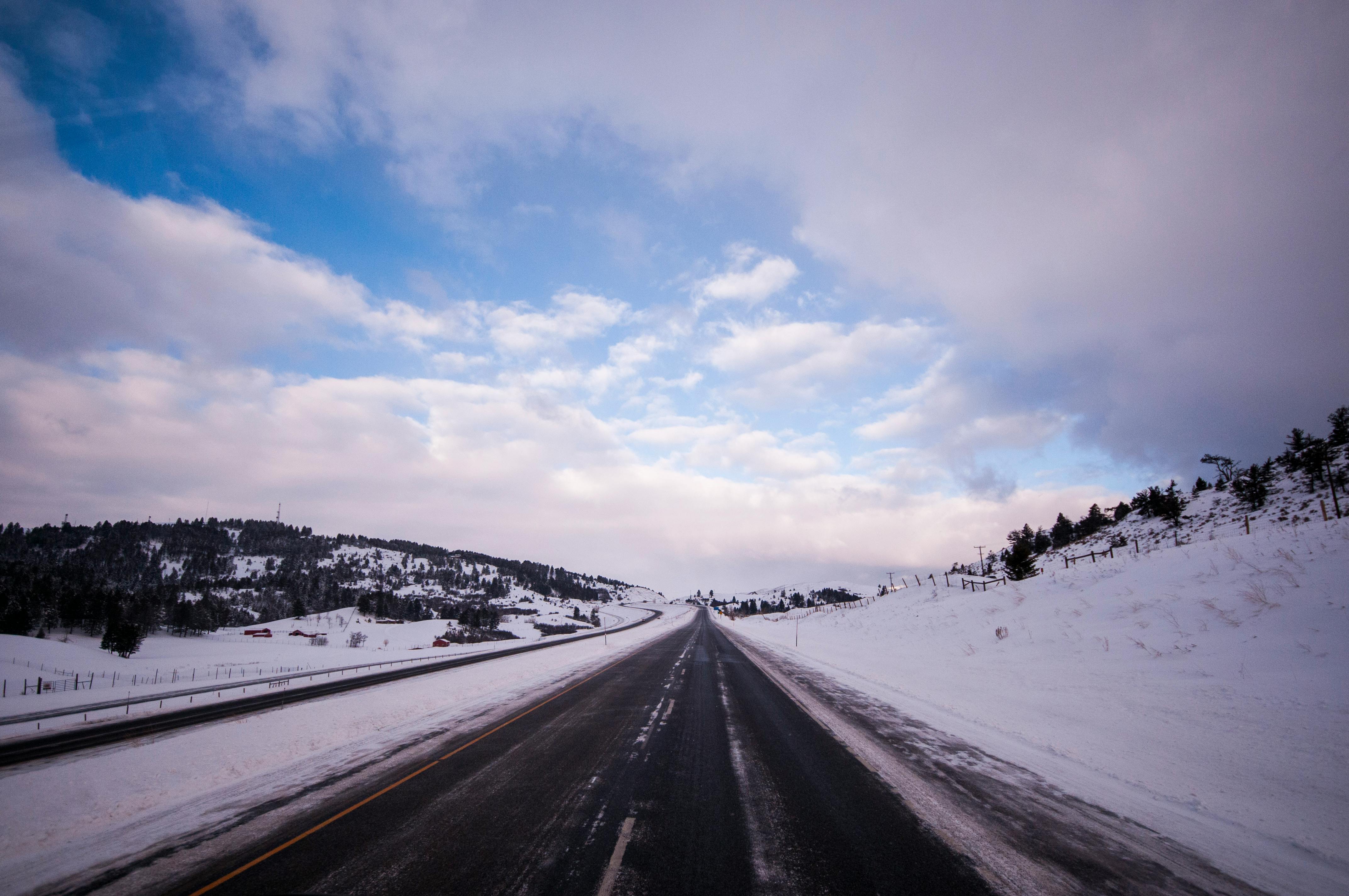 A deserted highway cuts through a snowy winter landscape under a blue sky.