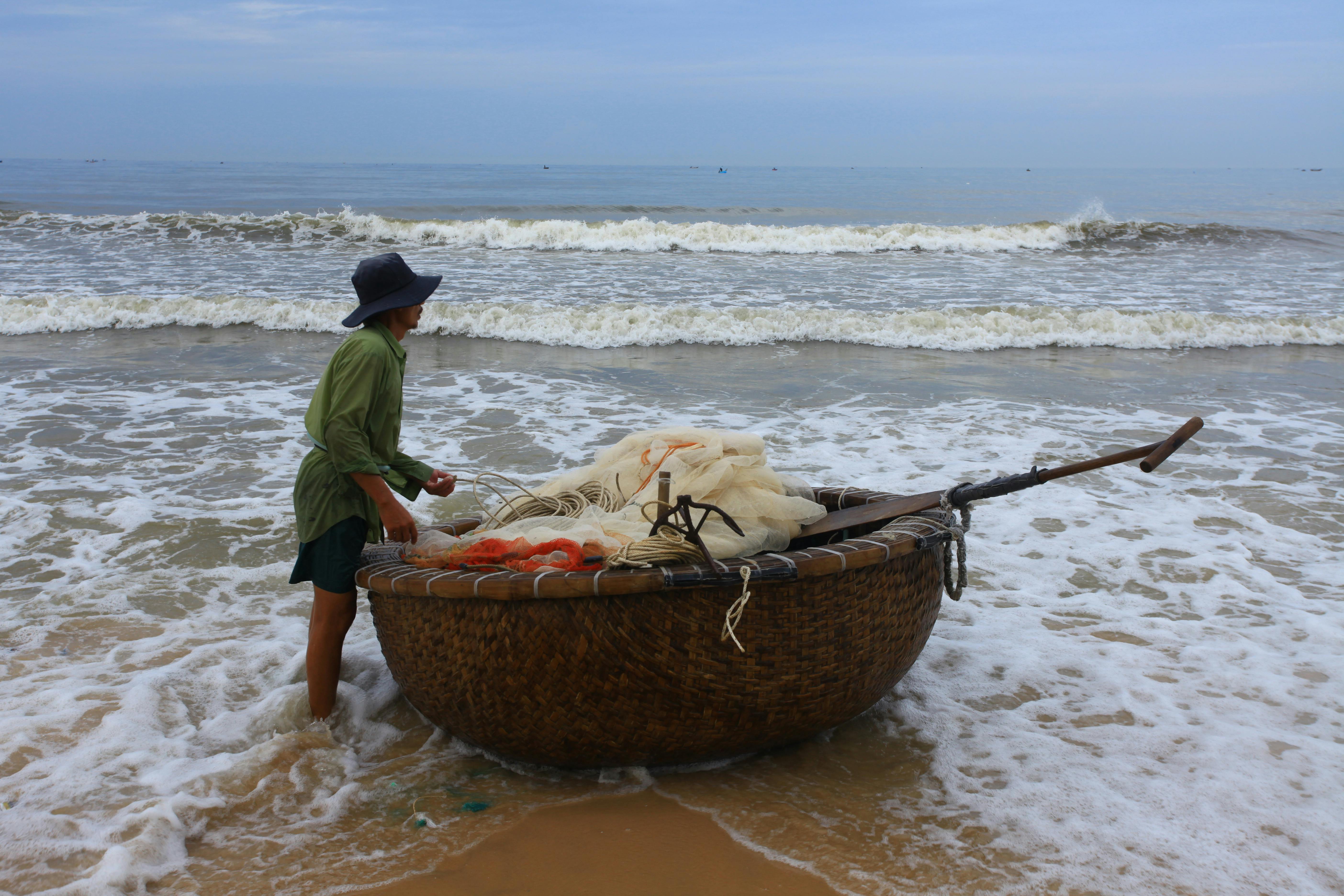 A fisherman with a reed boat prepares for fishing on a calm beach.